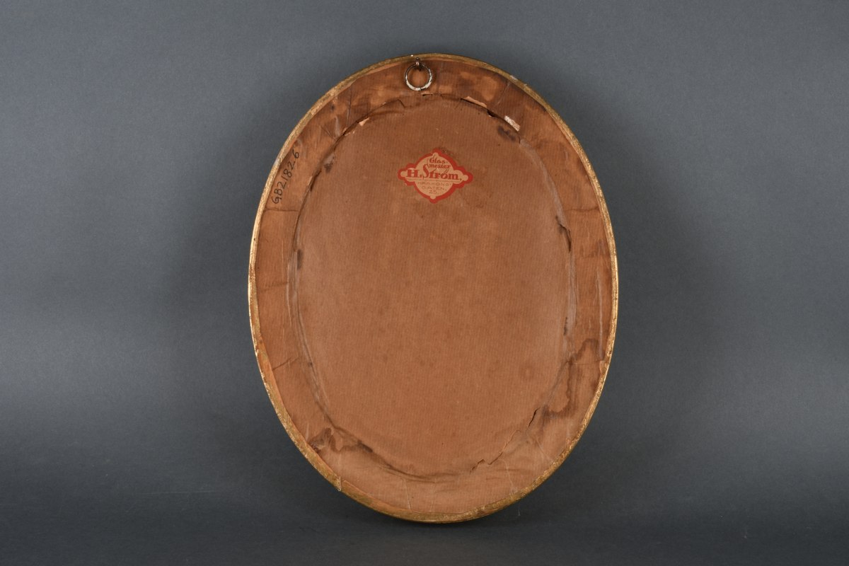 Innrammet svart-hvitt foto med oval form. Motivet viser portrett av en kvinne som ser forbi kamera. Hun har høy krage og oppsatt hår. Rammen er gullforgylt med dekorativ bord ytterst og perlebord innerst, samt beskyttende glass.