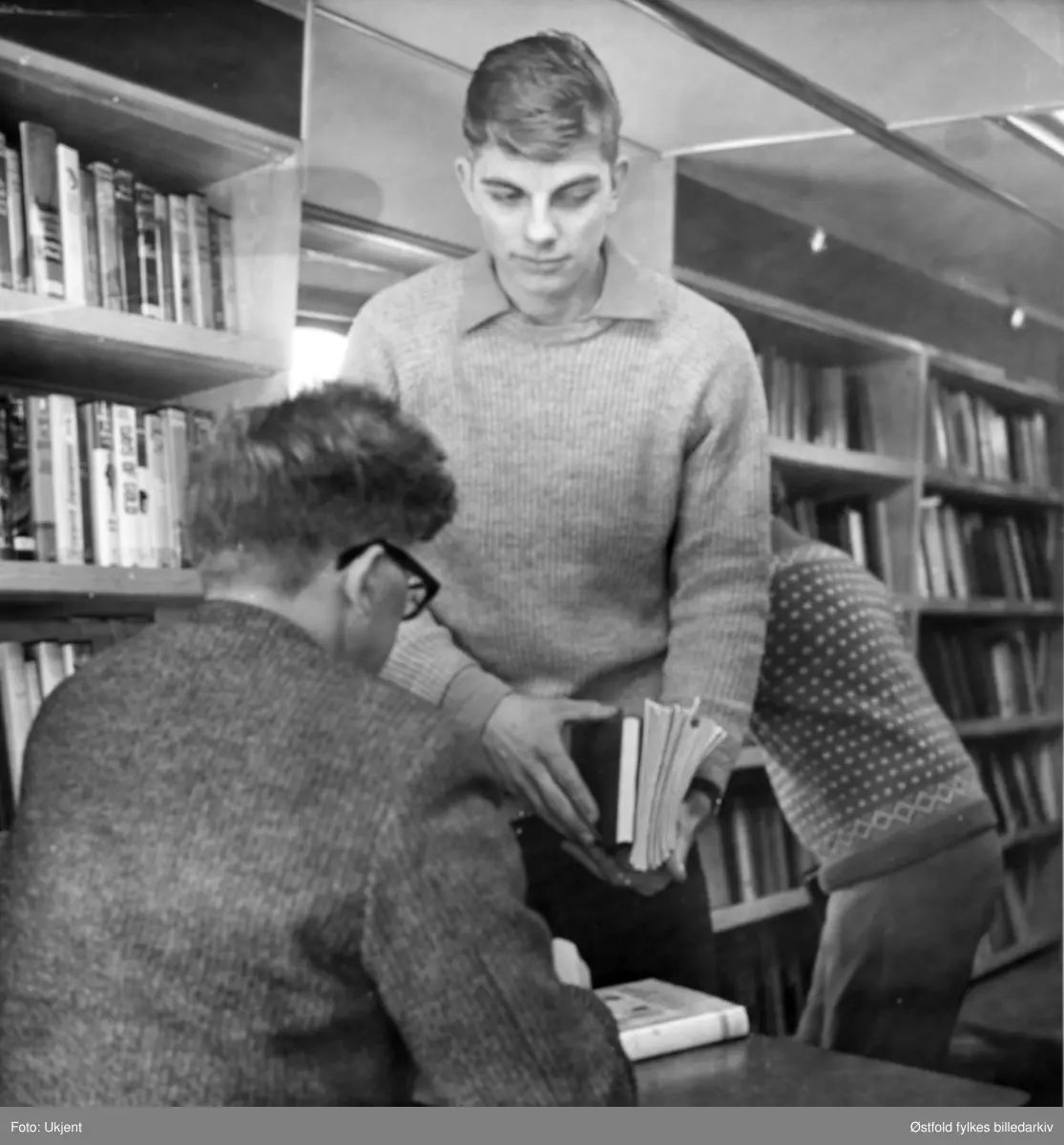 Fra bokbussen / biblioekbussen til ØStfold sentralebibliotek Ukjent sted. Boklåner (ukjent) og med ryggen til sjåfør og bibliotekfullmektig Viggo Nilsen.