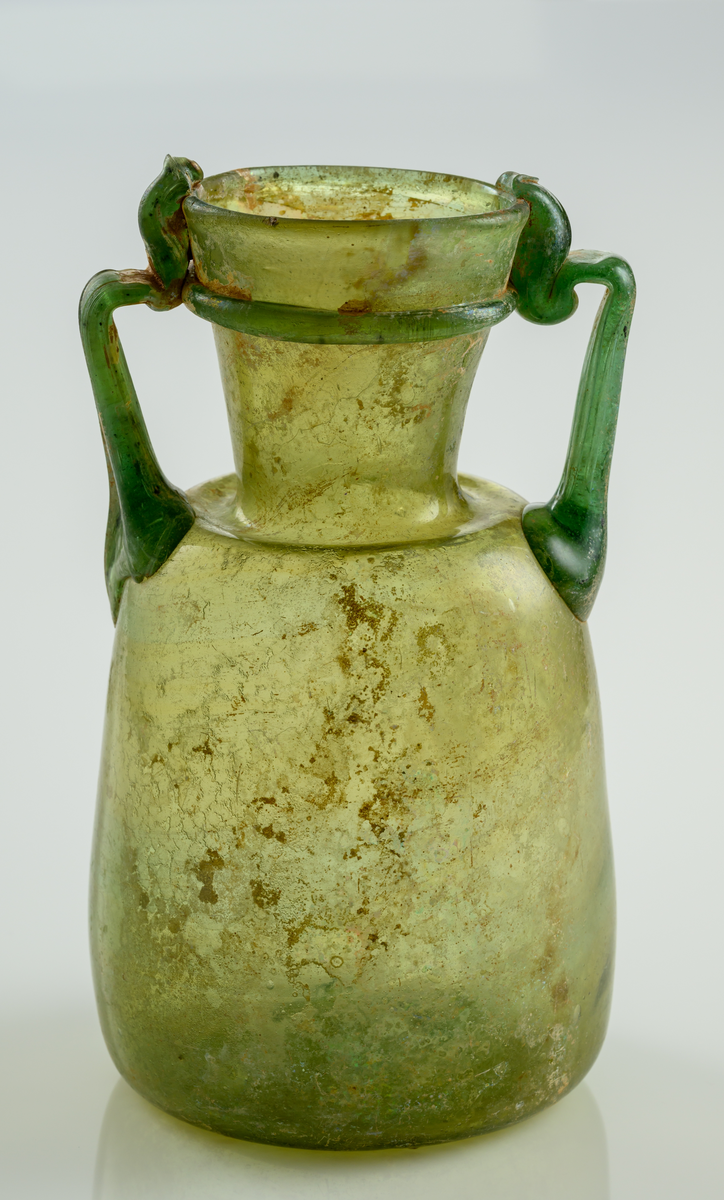Urna i gröntonat glas, med dubbla grepar. Svagt konisk nedre del som övergår i en bred hals som vidgar sig uppåt.