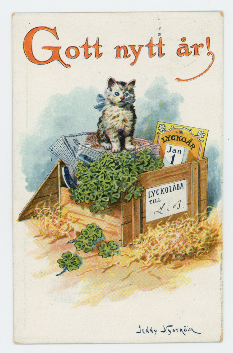 Nyårskort med motiv av en kattunge som sitter i en trälåda med diverse saker i. Ovanför katten finns texten "Gott nytt år!". Nere i högra hörnet finns illustratörens namnteckning: Jenny Nyström. Jenny Nyström (1854-1946) var en känd, svensk konstnär och illustratör. På baksidan finns ett orange 2-öres frimärke med tre kronor i oval. Kortet är poststämplat den 1 januari 1915.