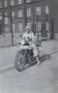 En kvinna sitter på en militär motorcykel framför en byggnad, omkring 1934-1937.

Text vid foto: 