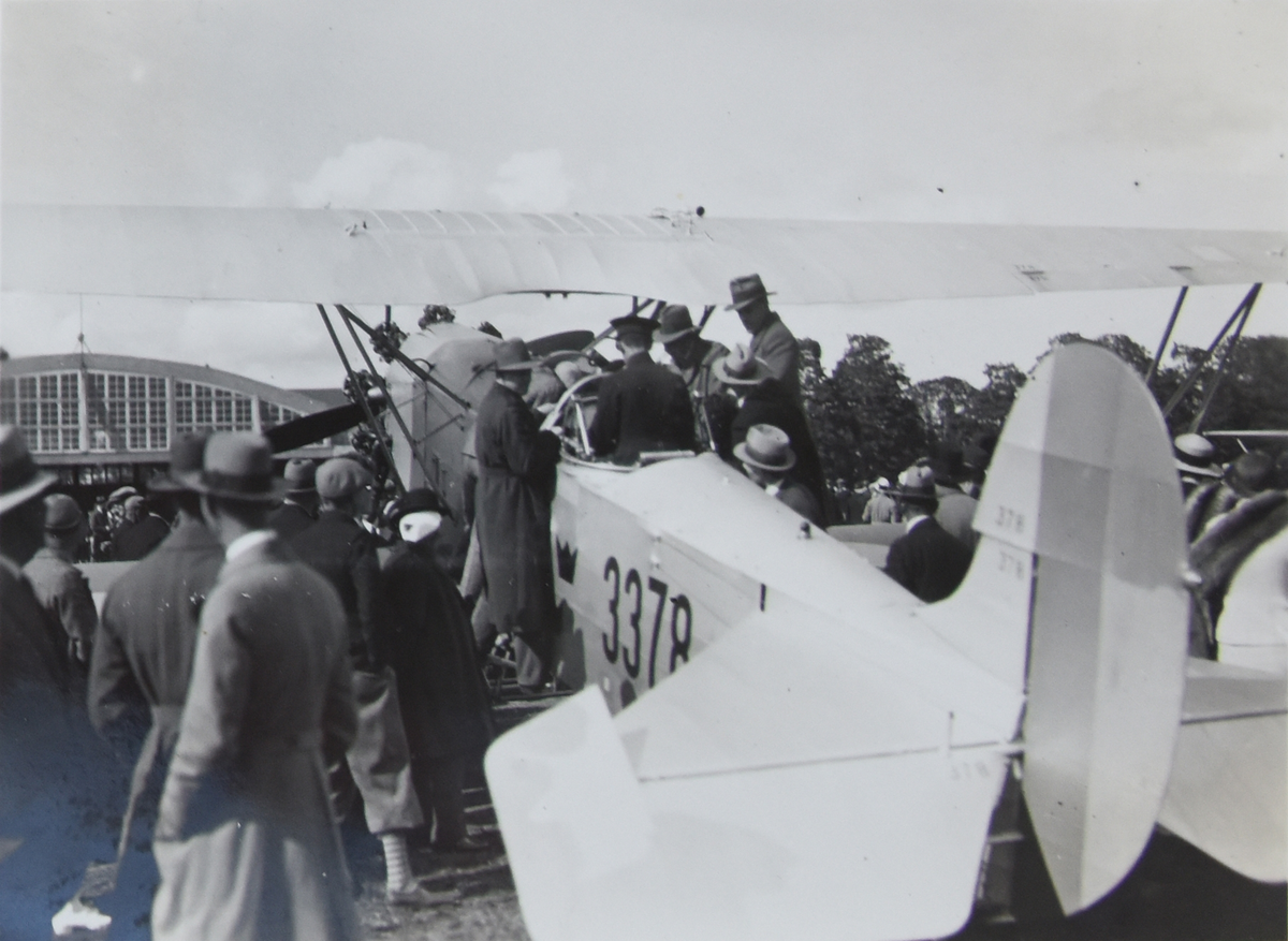 Förevisning av spaningsflygplan S 6 Fokker nummer 3378 under flygdag på F 3 Malmen, 1934. Folksamling vid flygplan, förare i sittbrunnen. Vy bakifrån.

Text vid foto: "Jag demonstrerar mitt flygplan"