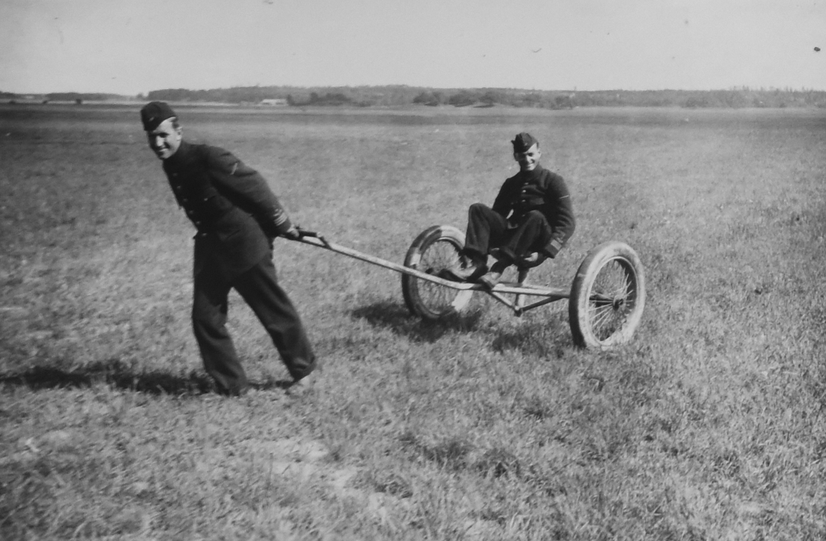 Två flygsoldater på ett flygfält omkring 1935. Den ene drar den andra med underhållsvagn för flygplan. Mannen till höger är Nils Olofs Svensson (senare Sefeldt). 

Text vid foto: "Västerås flygfält"