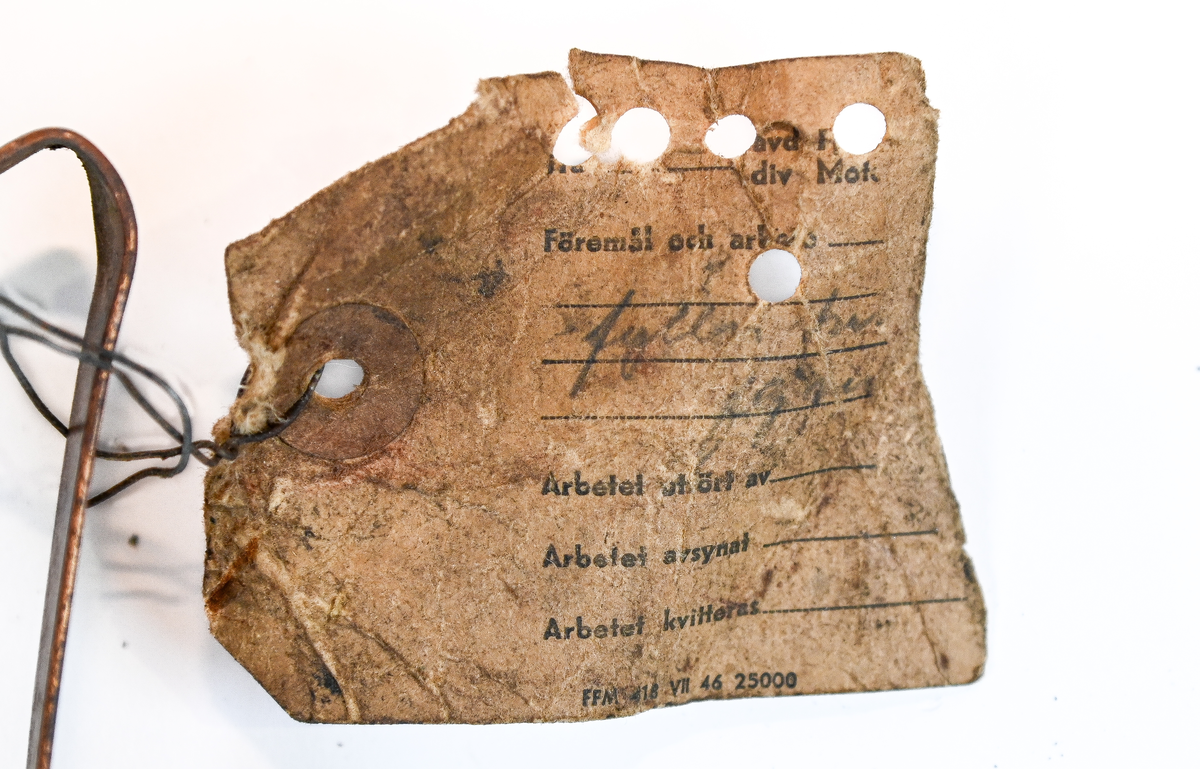 Brandsläckare i röd metall med väggstativ i järn. Brandsläckaren utlöstes genom att slå den nedre ventilen i marken. Väggstativet utgör en säkerhet för att undvika oönskade aktivering av brandsläckaren. På sidan av och runt om föremålet ser man rester av en etikett med engelsk text som agerar som instruktioner för användning. Texten är svår att läsa. På föremålet hittades en etikett med svensk text, okänt ursprung.