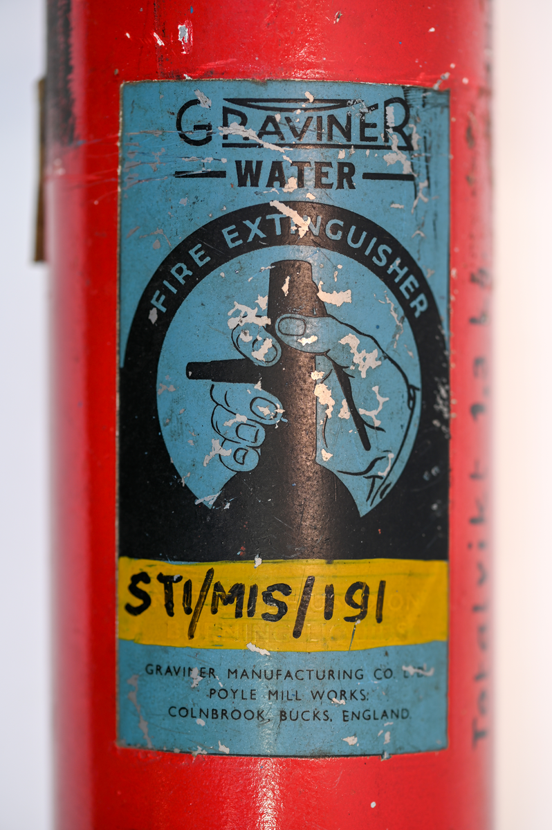 Brandsläckare i röd metall, med handtag och väggfäste, modell Graviner MK.27H. På föremålets framsida stor det information om tillverkaren och modellen och på baksidan användning och påfyllningsinformation, på engelska. Modell avsedd för användning med vatten. Föremålet fylldes på sist den 21 september 1955 i Sverige. Total vikt med laddning 1,3 kg.