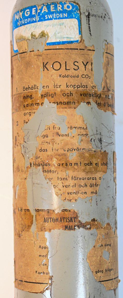 Kolsyreflaska i silverfärgad metall, förmodligen ansett som en del av en brandsläckare system. Flaskan är märkt som tillverkad av De Förenade Kolsyrefabrikernas AB 1/3/1952 och med sista inspektion av Swedish Airworks LTD 27/02/1974. På sidan finns det instruktion för hantering av föremålet som gasflaska på ena sidan och som brandsläckare på andra sidan. Fylld vikt: 1.31 kg. Prägling som attesterat att flaskan fick inspektion 1958, 1965 och 1972.