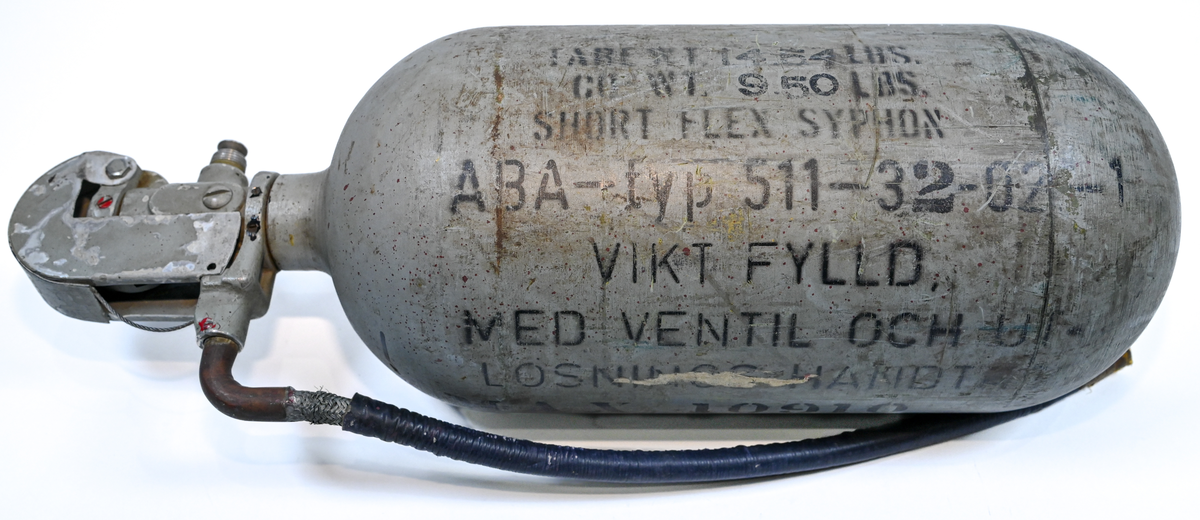 Kolsyresläckare i gråfärgad avrundad metall flaska med ventil, lösningshandtag och slang i fiber och läder, tillverkad av De Förenade Kolsyrefabrikernas AB. På föremålet står det ABA Typ-501-32-02-1. Tillsynsdatum präglat på flaskan 10/40 och 07/46.