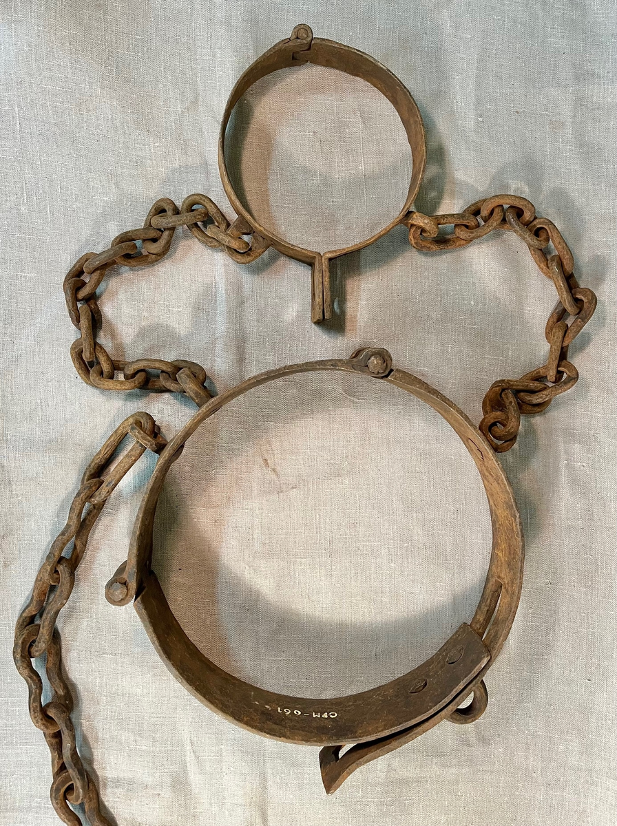 Svært kraftig fangejern bestående av halsring og midjejern. Halsringen er hengslet og festet tilmidjejernet med to lenker. Lenkene har 11 og 13 ledd. Midjejernet er tredelt, har to hengsler, og endestykker, det ene med tre hull, det andre med tre kramper, så jernet kan justeres etter fangens midjemål. Fra livringens bakside går en lenke på 25 ledd, for feste i vegg e.l.