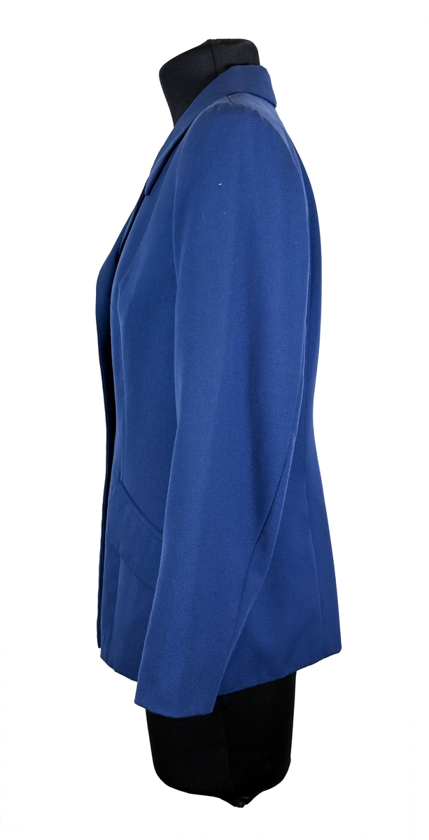 Kavaj i mörklbå ull- och polysterblandning till ämbetsdräkt för kvinnlig personal vid Luftfartsverket. Fodret är gjort i mörkblå polyester. Kavajen har två framfickor med lock som fortfarande är igensydda samt en innerficka vänster sida som stängs med plastknapp. Kavajen stängs med metallknappar med Luftfartsverkets logga i relief. 

På insidan ovanför innerfickan sitter en lapp med Luftfartsverkets logga samt information om tillverkare och designer. I anslutnings till den sitter en mindre lapp med storleksangivelser. Kavajen producerad av Confetti och designad av Morgan i storlek C42. På insidan i ena sidosömmen sitter ytterligare en lapp med tvättanvisningar och information om material och tillverkningsort. Kavajan är tillverkad i Estland. I denna lapp sitter en extra metallknapp samt en fasthäftad papperslapp med numret "8632" i tryck och "3/10" påskrivet i blått bläck.