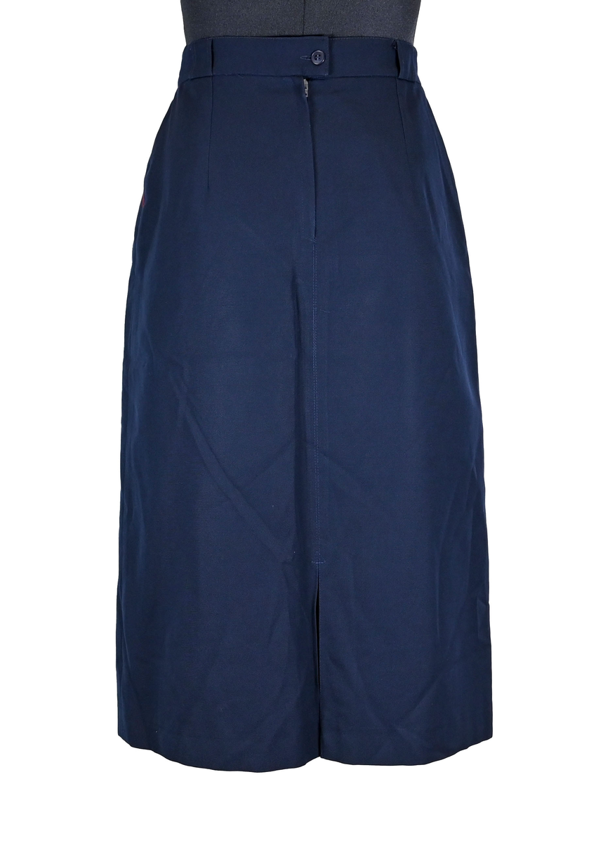 Kjol för flygbolagspersonal på Linjeflyg. Mörkblå snäv modell med slitsar och veck för vidd nertill. Med vinröda passpoaler på fickornas kanter. Märkt ”Linjeflyg”.