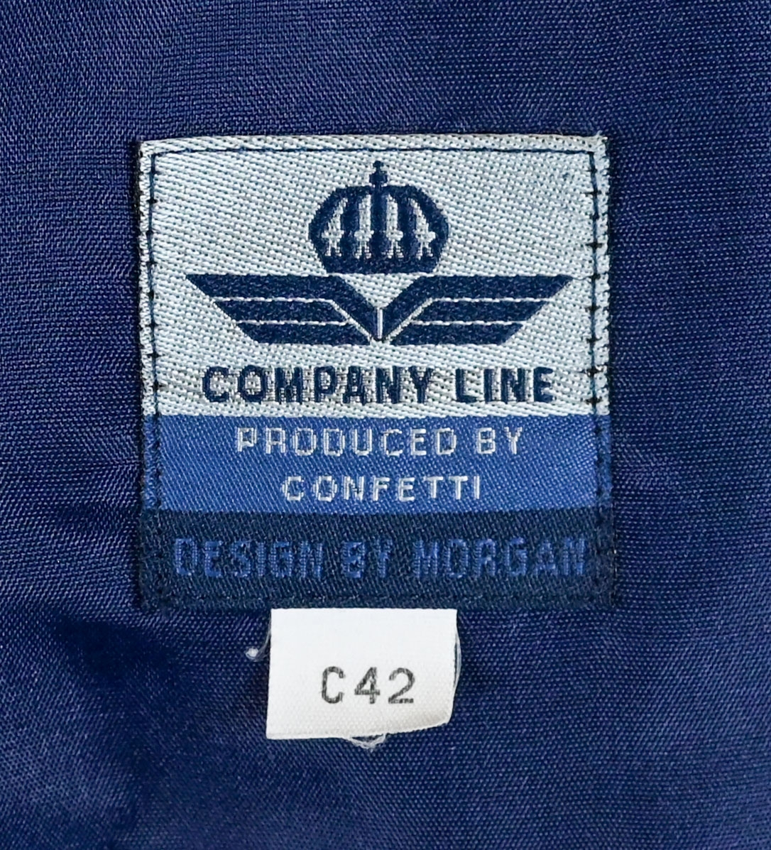 Kavaj i mörklbå ull- och polysterblandning till ämbetsdräkt för kvinnlig personal vid Luftfartsverket. Fodret är gjort i mörkblå polyester. Kavajen har två framfickor med lock som fortfarande är igensydda samt en innerficka vänster sida som stängs med plastknapp. Kavajen stängs med metallknappar med Luftfartsverkets logga i relief. 

På insidan ovanför innerfickan sitter en lapp med Luftfartsverkets logga samt information om tillverkare och designer. I anslutnings till den sitter en mindre lapp med storleksangivelser. Kavajen producerad av Confetti och designad av Morgan i storlek C42. På insidan i ena sidosömmen sitter ytterligare en lapp med tvättanvisningar och information om material och tillverkningsort. Kavajan är tillverkad i Estland. I denna lapp sitter en extra metallknapp samt en fasthäftad papperslapp med numret "8632" i tryck och "3/10" påskrivet i blått bläck.