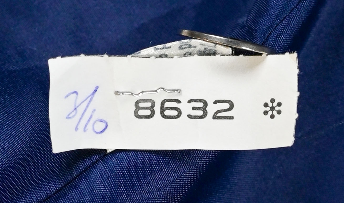 Kavaj i mörklbå ull- och polysterblandning till ämbetsdräkt för kvinnlig personal vid Luftfartsverket. Fodret är gjort i mörkblå polyester. Kavajen har två framfickor med lock som fortfarande är igensydda samt en innerficka vänster sida som stängs med plastknapp. Kavajen stängs med metallknappar med Luftfartsverkets logga i relief. 

På insidan ovanför innerfickan sitter en lapp med Luftfartsverkets logga samt information om tillverkare och designer. I anslutnings till den sitter en mindre lapp med storleksangivelser. Kavajen producerad av Confetti och designad av Morgan i storlek C42. På insidan i ena sidosömmen sitter ytterligare en lapp med tvättanvisningar och information om material och tillverkningsort. Kavajan är tillverkad i Estland. I denna lapp sitter en extra metallknapp samt en fasthäftad papperslapp med numret "8632" i tryck och "3/10" påskrivet i blått bläck.