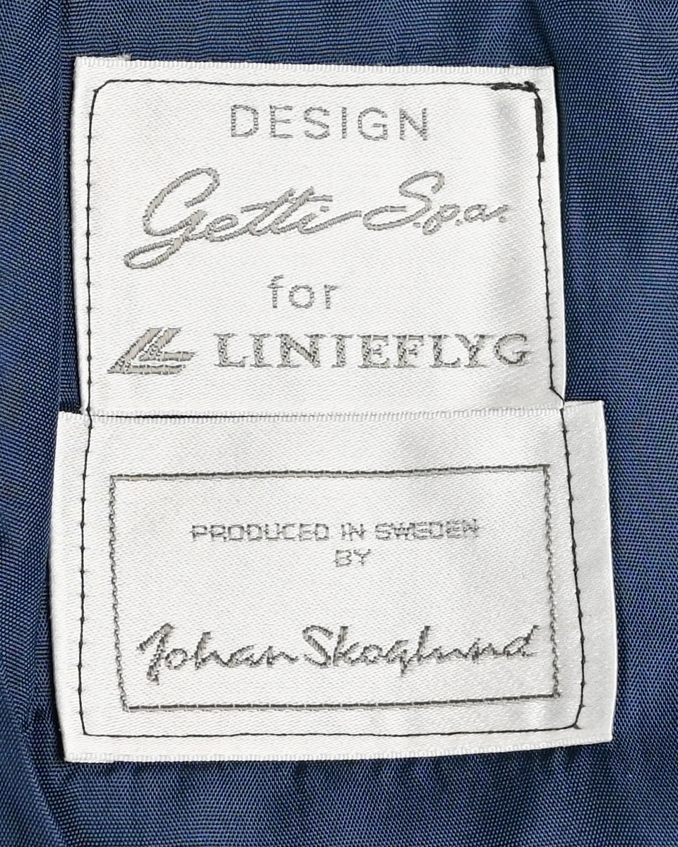 Kjol för flygbolagspersonal på Linjeflyg. Mörkblå snäv modell med slitsar och veck för vidd nertill. Med vinröda passpoaler på fickornas kanter. Märkt ”Linjeflyg”.