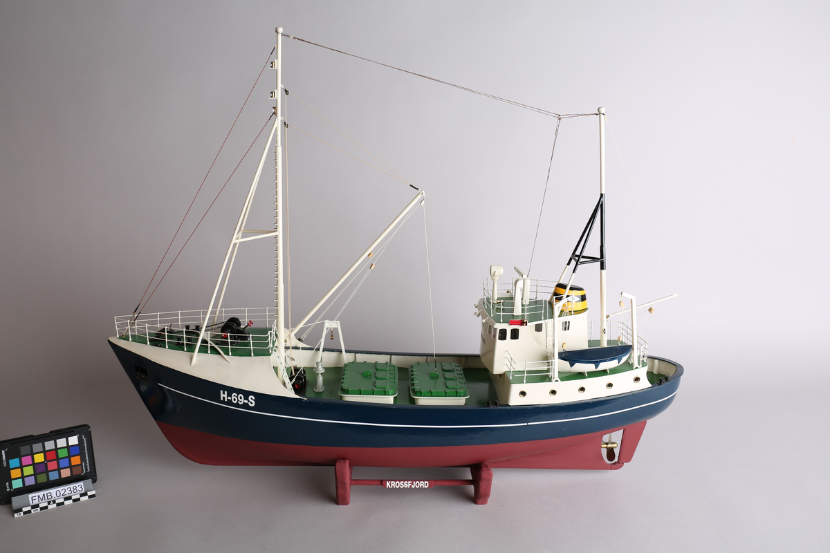 Modell av moderne fiskeskøyte, med blokk og lastebom. Bygget med shelterdekk. Bygget i malt tre, med detaljer i metall.  En livbåt.