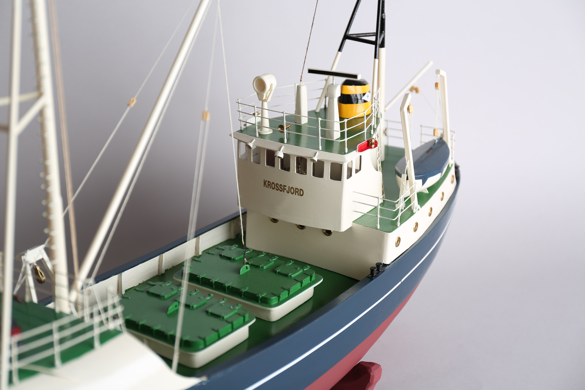 Modell av moderne fiskeskøyte, med blokk og lastebom. Bygget med shelterdekk. Bygget i malt tre, med detaljer i metall.  En livbåt.
