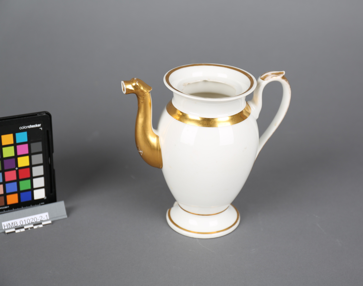 Kanne. Høy, smal, Høy tut formet som et dyrehode. Høyt svunget hank med bladform. Utfallende fot og munning. Forgylte ringer rundt foten, øverst på korpus og minningen, samt delvis forgylt tut og hank. Avslått skår på foten. Lokkring i numming flere avslåtte skår. Alle skår mangler.