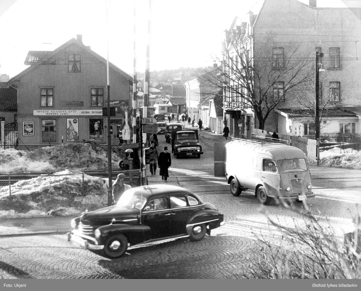 Jeløgata i Moss 1960-61. Før bygging av ny Rådhusbru. Jernbanegata, Stengata og Jeløygata. Ca. 1960. Til venstre forretningen Trygve Nilssens Eftf. Martha Lyby, kolonial og skipshandel. Grand Hotel til høyre. I forgrunnen en Opel Kapitän, 1950-53 modell. Lastebilen er en amerikansk Ford 1956, til høyre en Renault kassebil.