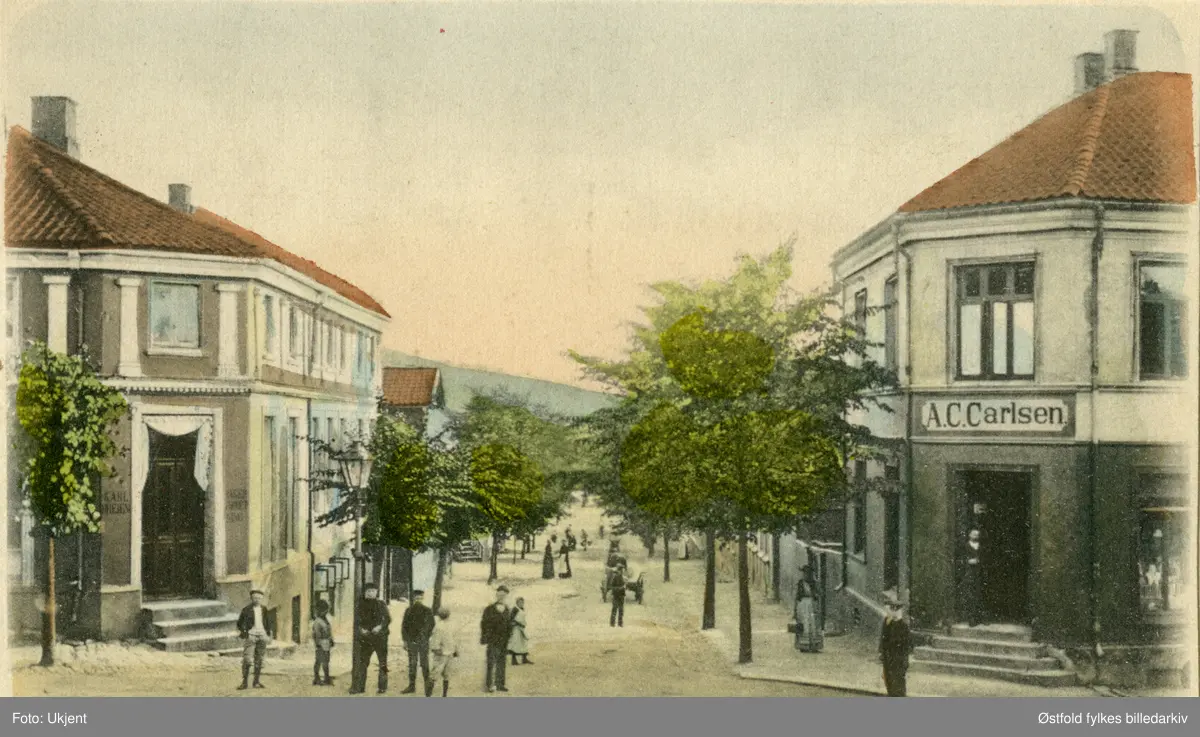 Værlegata i Moss. Ca. 1910.  På høyre gatehjørne A. C. Carlsen, kolonialforretning i Nyquists gate 21. Til venstre Nyquists gate 29. med forretningen til Carl ..heien (senere Selmers Bakeri (1907-10). 
Kolorert postkort.