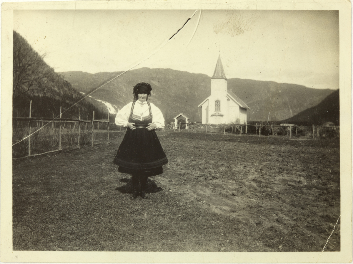 Setesdal. Kvinne i Setesdalsdrakt.  Austad kyrkje i bakgrunnen.