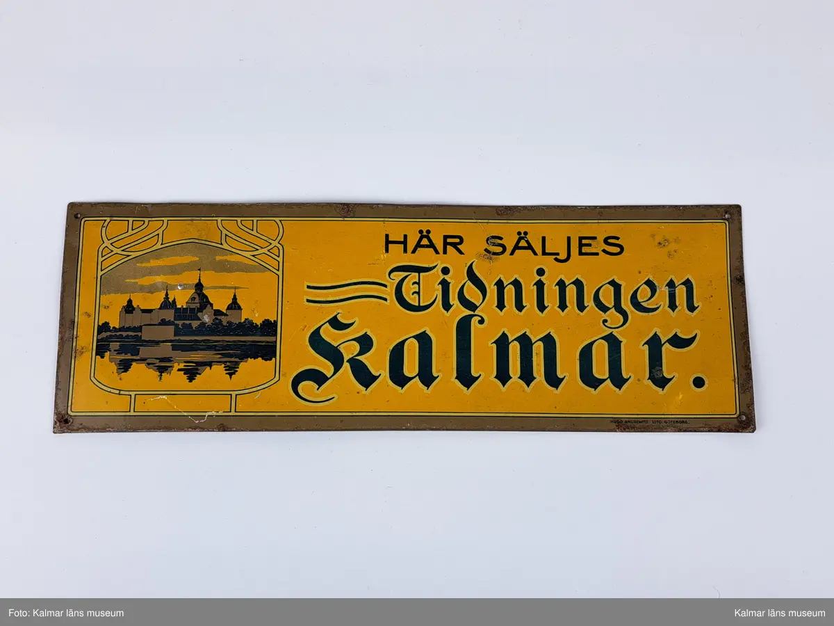 KLM 46850. Skylt. Av plåt. Gul bakgrund med bild av Kalmar slott i svart och grått. Text i svart och blått: HÄR SÄLJES Tidningen Kalmar. Tryck: HUGO BRUSEWITZ LITO. GÖTEBORG.