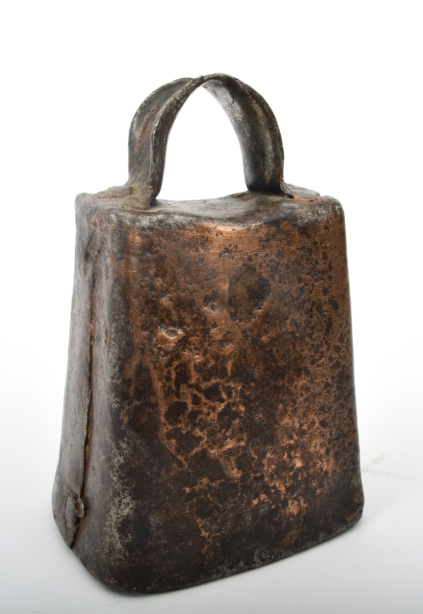 Frå Martin Sælid sin handskrivne katalog:
"Kubjølle av jern, brasa med ei blanding av kopar og messing. Den har ei totalhøgde av 11 cm og opningen under er 7,8 x 5,6 cm. Det er slitt hul mitt oppe på bjøllehanken. Eg kjøpte den på auksjon på Beito 1963"