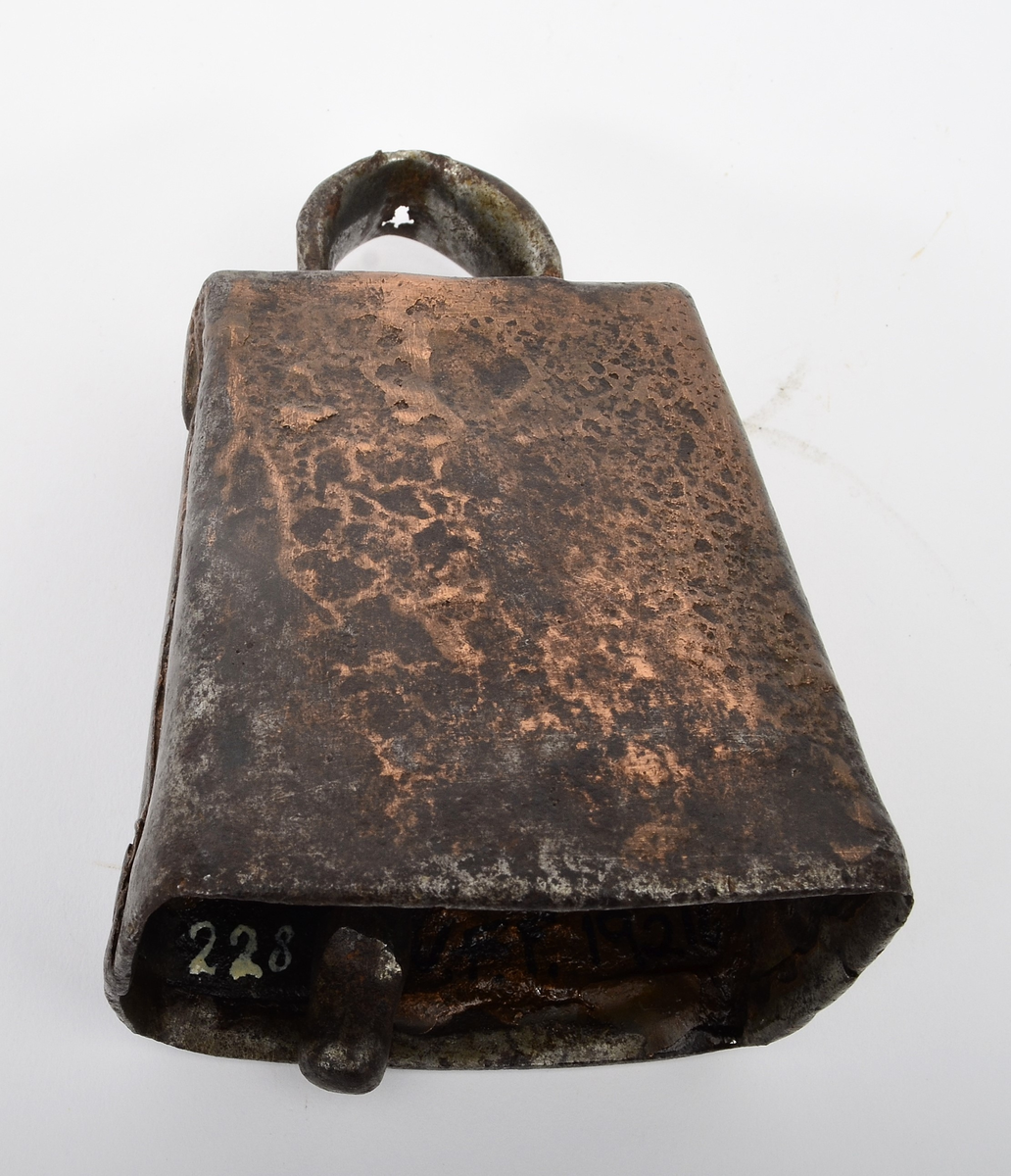 Frå Martin Sælid sin handskrivne katalog:
"Kubjølle av jern, brasa med ei blanding av kopar og messing. Den har ei totalhøgde av 11 cm og opningen under er 7,8 x 5,6 cm. Det er slitt hul mitt oppe på bjøllehanken. Eg kjøpte den på auksjon på Beito 1963"