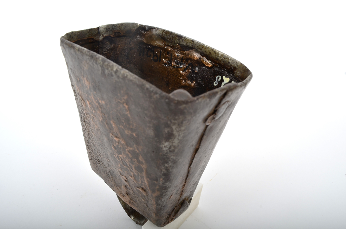 Frå Martin Sælid sin handskrivne katalog:
"Kubjølle av jern, brasa med ei blanding av kopar og messing. Den har ei totalhøgde av 11 cm og opningen under er 7,8 x 5,6 cm. Det er slitt hul mitt oppe på bjøllehanken. Eg kjøpte den på auksjon på Beito 1963"