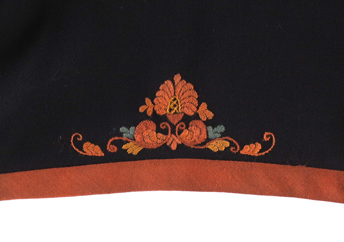 Trøye til Vest-Telemark bunad i ullstoff med rosesaum i jordfargar. Trøya har eit kuftespenne i filigramsrbeid øverst i opninga framme. Ståkrage og splittar ved handledda.