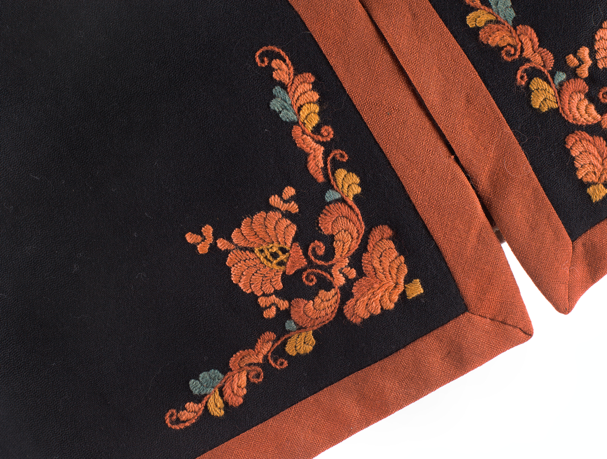 Trøye til Vest-Telemark bunad i ullstoff med rosesaum i jordfargar. Trøya har eit kuftespenne i filigramsrbeid øverst i opninga framme. Ståkrage og splittar ved handledda.