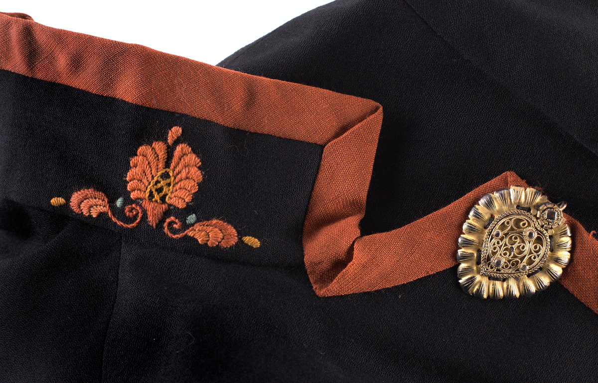 Trøye til Vest-Telemark bunad i ullstoff med rosesaum i jordfargar. Trøya har eit kuftespenne i filigramsrbeid øverst i opninga framme. Ståkrage og splittar ved handledda.