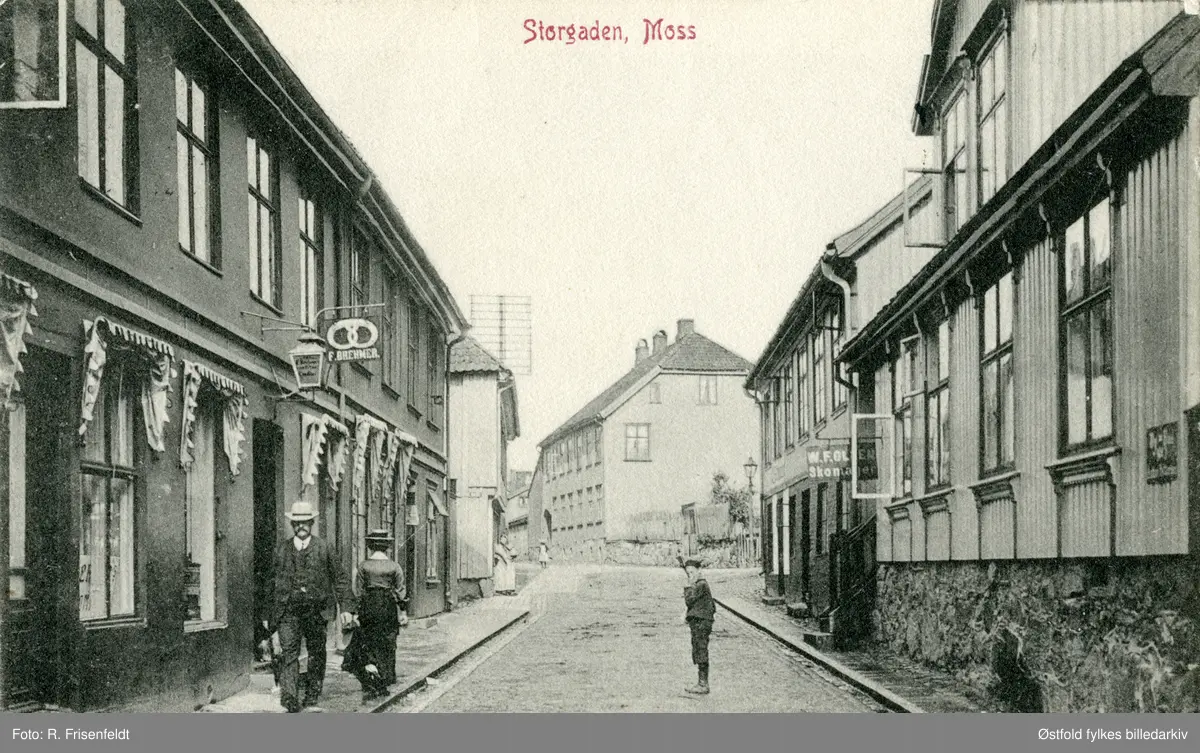 Storgata i Moss ca. 1910.  Til venstre F. Brehmer Bageri & Conditori i Storgata 16 ca. 1910. Til høyre skomaker W. F. Olsen. 
Heiberggården i bakgrunnen, seinere Moss Handelstands Forenings bygning. Postkort.