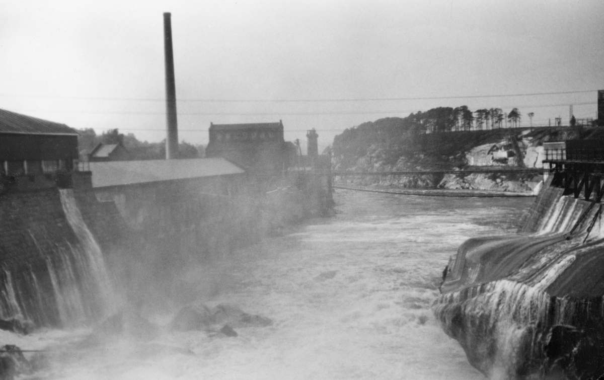 Sarpsfossen (navnet har også vært stavet «Sarpefossen» eller bare «Sarpen») i Nedre Glomma, fotografert i medstrøms retning en gråværsdag i 1943. Dette vannrike, drøyt 20 meter høye fossefallet har gitt engergi til mye industriell virksomhet. Bak disen fra fossefallet, til venstre på dette bildet, skimter vi noe av bygningsmassen på Hafslund Sulfitfabrik, en cellulosefabrikk som ble etablert i 1873-74, men kraftig ombygd i 1886. Denne fabrikken ble oppkjøpt av The Kellner-Partington Paper Pulp Co. Ltd., som eide nabobedriften på «Borregaard-sida» av elva, i 1905. De virksomhetene dette selskapet hadde ved Sarpsfossen ble overtatt av norske investorer under navnet A/S Borregaard i 1918. Dette selskapet videreførte celluloseproduksjonen på Hafslund, og fabrikken var i drift med en årsproduksjon på om lag 18 000 tonn da dette fotografiet ble tatt. I 1947 ble denne produksjonen avviklet. Seinere ble bygningsmassen oppkjøpt av A/S Sarpsborg Pap- og Papirindustri, som fra 1955 satte i gang produksjon av emballasjekartong med returpapir som råstoff.