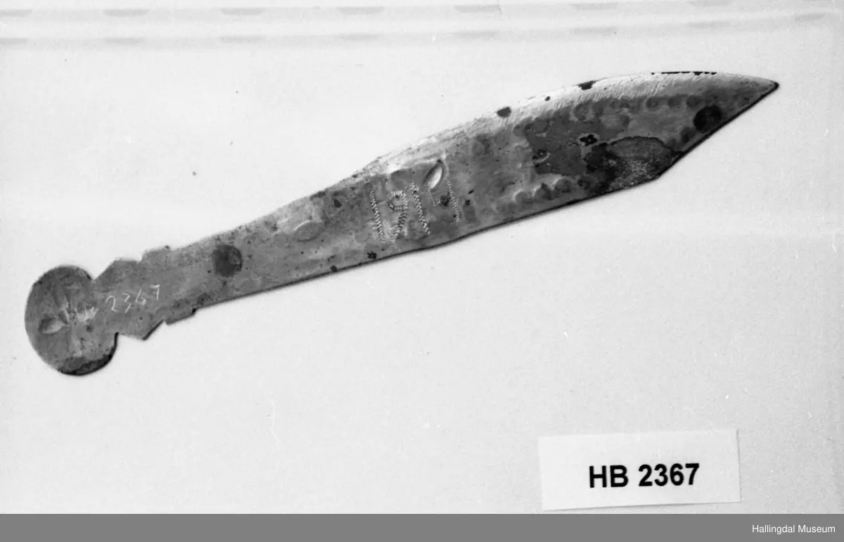 Messing, gravert dekor, blomster og ranker. Årstallet 1914 bak. L: 16 cm, bredde: 2,5 cm.