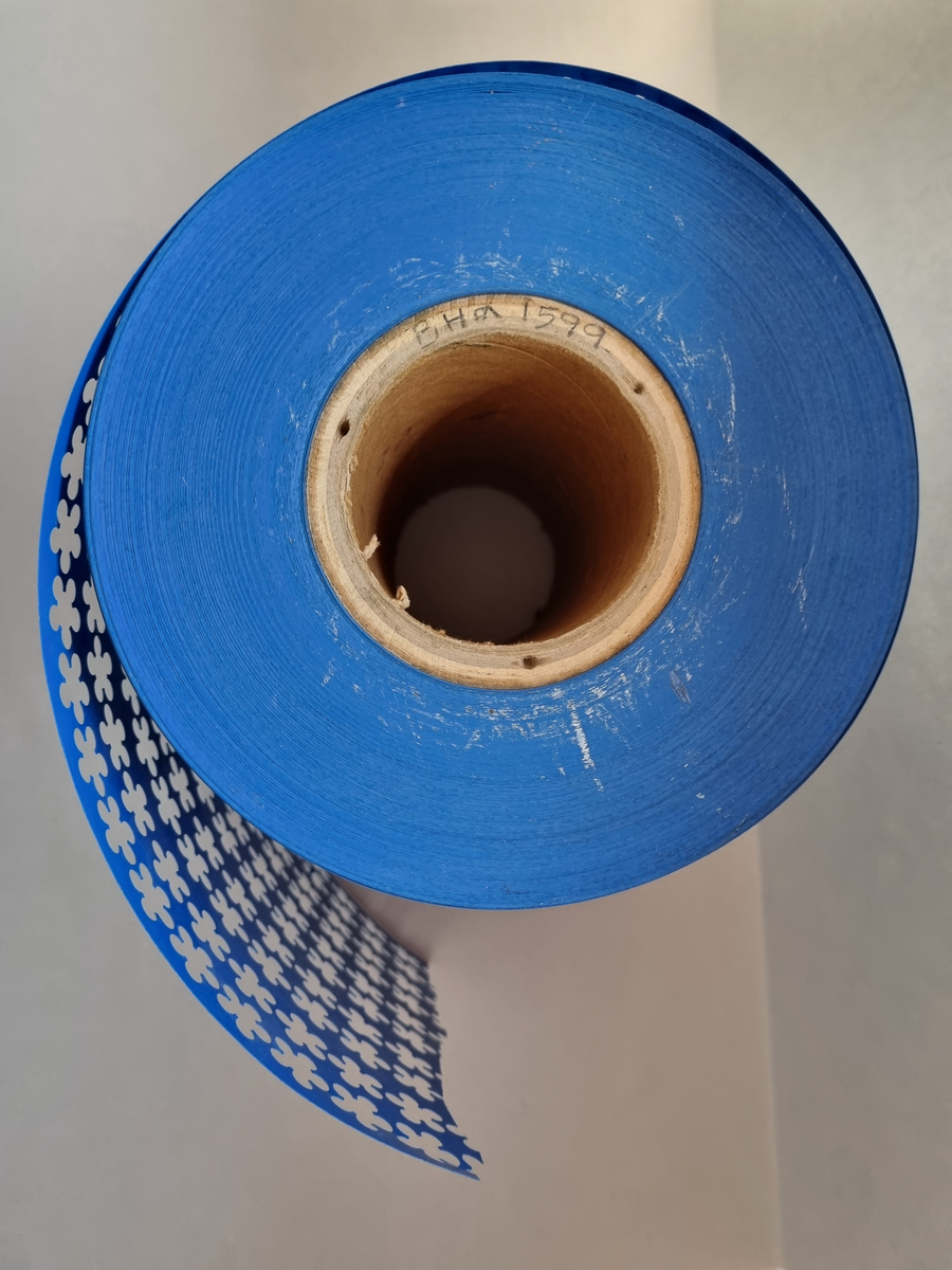 Rulle som suttit i majblommemaskin och är en restprodukt av majblommetillverkning. Blå.  Under en period såldes bordslöpare av detta material.