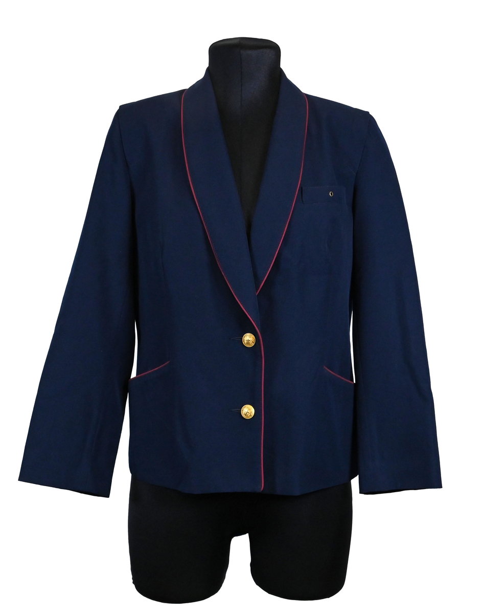 Kavaj, uniform, dammodell. Mörkblå tyg av 80% ull och 20 % polyester. Enkelknäppning med två guldfärgade metallknappar. Två midjefickor och en bröstficka på vänster sida, samt en innerficka. Kavajslaget och fickornas kanter har vinröda passpoaler. Design av Getti S.P.A.