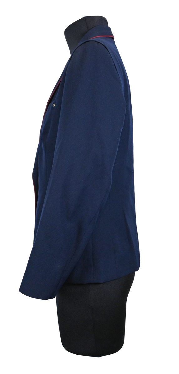 Kavaj, uniform, dammodell. Mörkblå tyg av 80% ull och 20 % polyester. Enkelknäppning med två guldfärgade metallknappar. Två midjefickor och en bröstficka på vänster sida, samt en innerficka. Kavajslaget och fickornas kanter har vinröda passpoaler. Design av Getti S.P.A.