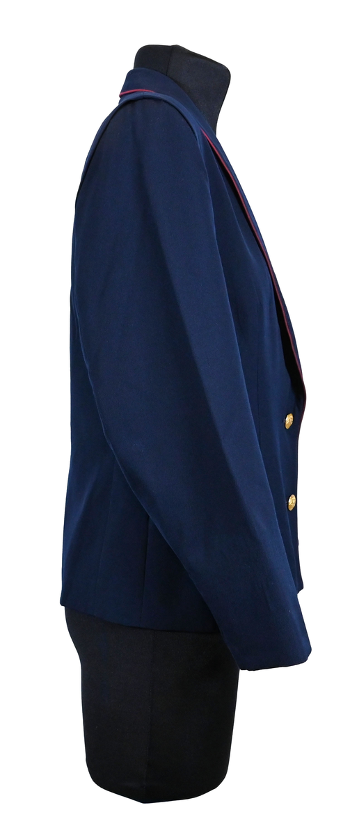 Kavaj, uniform, dammodell. Mörkblå tyg av 80% ull och 20 % polyester. Enkelknäppning med två guldfärgade metallknappar. Två midjefickor och en bröstficka på vänster sida, samt en innerficka. Kavajslaget och fickornas kanter har vinröda passpoaler. Design av Getti S.P.A.