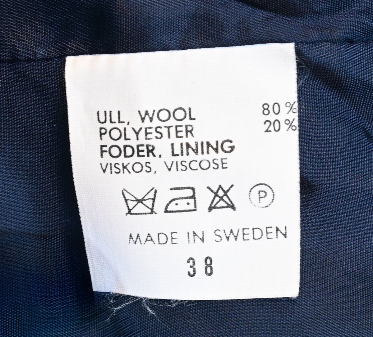 Kavaj, uniform, dammodell. Mörkblå tyg av 80% ull och 20 % polyester. Enkelknäppning med två guldfärgade metallknappar. Två midjefickor och en bröstficka på vänster sida, samt en innerficka. Kavajslaget och fickornas kanter har vinröda passpoaler. Design av Getti S.P.A.