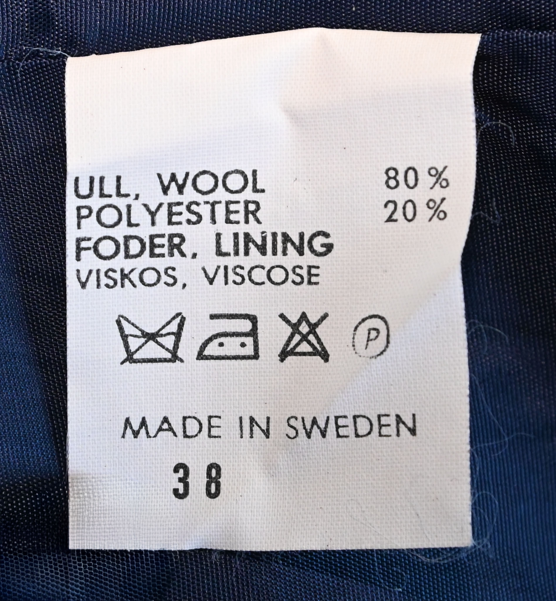 Kavaj, uniform, dammodell. Mörkblå tyg av 80% ull och 20 % polyester. Enkelkläppning med två guldfärgade knappar och tre rader av guldgaloner vid vardera ärmslut. Två midjefickor och en bröstficka på vänster sida. Kavajslaget och fickornas kanter har vinröda passpoaler. Design av Getti S.P.A.