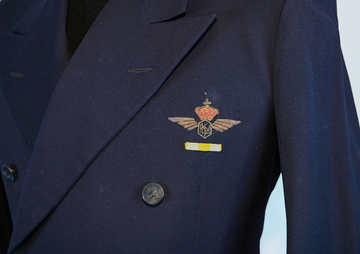 Kavaj i herrmodell, uniform från flygbolaget KLM Royal Dutch Airlines. Har tidigare tillhört Carl Gustaf Von Rosen. Mörkblå ylle med dubbelknäppning. Med KLMs emblem på vänster sida samt två galoner vid var ärmslut.