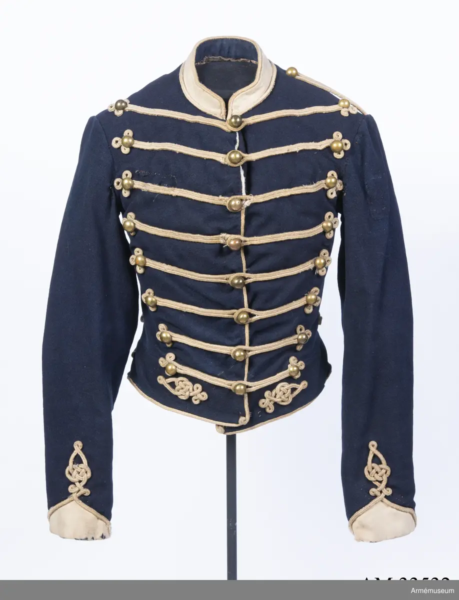 Blå dolma m/1846 med platta vita snören m/1851.

Dolman är sydd av mörkblått kommisskläde, med liten ståndkrage och ärmuppslag av vitt kläde. Helfodrad med vitt bomullstyg.
Plagget är kroppsnära, och är konstruerat med fram- och sidstycken i ett, sidstycken bak, samt helt bakstycke som går ner i en avkapad spets mitt bak. Det har midjesöm och litet skört som fortsätter bak och bildar veck vid sidsömmen. Ärmarna är ensömsärmar eller S-ärmar med fasta vita ärmuppslag som slutar i en spets upptill, och har ärmsprund som knäpps med hysk och hake.
Tvärs över bröstet löper 8 rader med snörmakerier med 3 lodräta knapprader med 8 knappar i varje. De yttre raderna har kullriga nappar medan mittenraden har klotknappar. Samtliga knappar är av mässing. Snörmakerierna är gjorda av vita fyrkantsnören, så kallade platta snören, av ull.
Plagget bär spår av att vara omsytt; bland annat är ärmarna förlängda nertill och en lång kil är iskarvad från ärmhålet till underärmen på båda ärmar. Framtill syns iskarvade kilar nertill. Det är även hårt slitet, och har flera lagade revor som uppstått under dess användningstid samt ett lappat hål på vänster ärmkulle framtill.
Innerficka i vänster framstycke, samt bröstfickor på båda sidor på utsidan, dolda under snörmakerierna.
Plagget är märkt för hand med skrivstil i ryggens fodersida, med bokstäverna W:N:S No 73, vilket troligen står för Westra Närkes Skvadron, soldatnummer 73.
På baksidan pryds dolman av snören längs med sidsömmarna som slutar i en knut upptill, samt med snörmakerier på skörtet, bland annat i form av en spiral. Även dolmans nederkant, framkant och ärmarnas nederkant pryds av snören.
