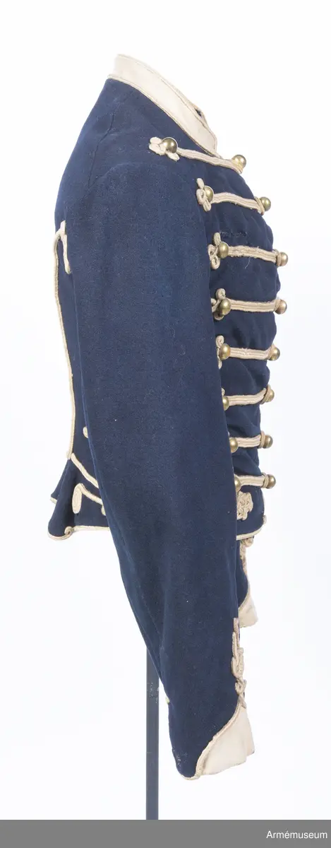 Blå dolma m/1846 med platta vita snören m/1851.

Dolman är sydd av mörkblått kommisskläde, med liten ståndkrage och ärmuppslag av vitt kläde. Helfodrad med vitt bomullstyg.
Plagget är kroppsnära, och är konstruerat med fram- och sidstycken i ett, sidstycken bak, samt helt bakstycke som går ner i en avkapad spets mitt bak. Det har midjesöm och litet skört som fortsätter bak och bildar veck vid sidsömmen. Ärmarna är ensömsärmar eller S-ärmar med fasta vita ärmuppslag som slutar i en spets upptill, och har ärmsprund som knäpps med hysk och hake.
Tvärs över bröstet löper 8 rader med snörmakerier med 3 lodräta knapprader med 8 knappar i varje. De yttre raderna har kullriga nappar medan mittenraden har klotknappar. Samtliga knappar är av mässing. Snörmakerierna är gjorda av vita fyrkantsnören, så kallade platta snören, av ull.
Plagget bär spår av att vara omsytt; bland annat är ärmarna förlängda nertill och en lång kil är iskarvad från ärmhålet till underärmen på båda ärmar. Framtill syns iskarvade kilar nertill. Det är även hårt slitet, och har flera lagade revor som uppstått under dess användningstid samt ett lappat hål på vänster ärmkulle framtill.
Innerficka i vänster framstycke, samt bröstfickor på båda sidor på utsidan, dolda under snörmakerierna.
Plagget är märkt för hand med skrivstil i ryggens fodersida, med bokstäverna W:N:S No 73, vilket troligen står för Westra Närkes Skvadron, soldatnummer 73.
På baksidan pryds dolman av snören längs med sidsömmarna som slutar i en knut upptill, samt med snörmakerier på skörtet, bland annat i form av en spiral. Även dolmans nederkant, framkant och ärmarnas nederkant pryds av snören.