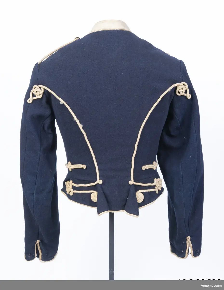 Blå dolma m/1846 med platta vita snören m/1851.

Dolman är sydd av mörkblått kommisskläde, med liten ståndkrage och ärmuppslag av vitt kläde. Helfodrad med vitt bomullstyg.
Plagget är kroppsnära, och är konstruerat med fram- och sidstycken i ett, sidstycken bak, samt helt bakstycke som går ner i en avkapad spets mitt bak. Det har midjesöm och litet skört som fortsätter bak och bildar veck vid sidsömmen. Ärmarna är ensömsärmar eller S-ärmar med fasta vita ärmuppslag som slutar i en spets upptill, och har ärmsprund som knäpps med hysk och hake.
Tvärs över bröstet löper 8 rader med snörmakerier med 3 lodräta knapprader med 8 knappar i varje. De yttre raderna har kullriga nappar medan mittenraden har klotknappar. Samtliga knappar är av mässing. Snörmakerierna är gjorda av vita fyrkantsnören, så kallade platta snören, av ull.
Plagget bär spår av att vara omsytt; bland annat är ärmarna förlängda nertill och en lång kil är iskarvad från ärmhålet till underärmen på båda ärmar. Framtill syns iskarvade kilar nertill. Det är även hårt slitet, och har flera lagade revor som uppstått under dess användningstid samt ett lappat hål på vänster ärmkulle framtill.
Innerficka i vänster framstycke, samt bröstfickor på båda sidor på utsidan, dolda under snörmakerierna.
Plagget är märkt för hand med skrivstil i ryggens fodersida, med bokstäverna W:N:S No 73, vilket troligen står för Westra Närkes Skvadron, soldatnummer 73.
På baksidan pryds dolman av snören längs med sidsömmarna som slutar i en knut upptill, samt med snörmakerier på skörtet, bland annat i form av en spiral. Även dolmans nederkant, framkant och ärmarnas nederkant pryds av snören.