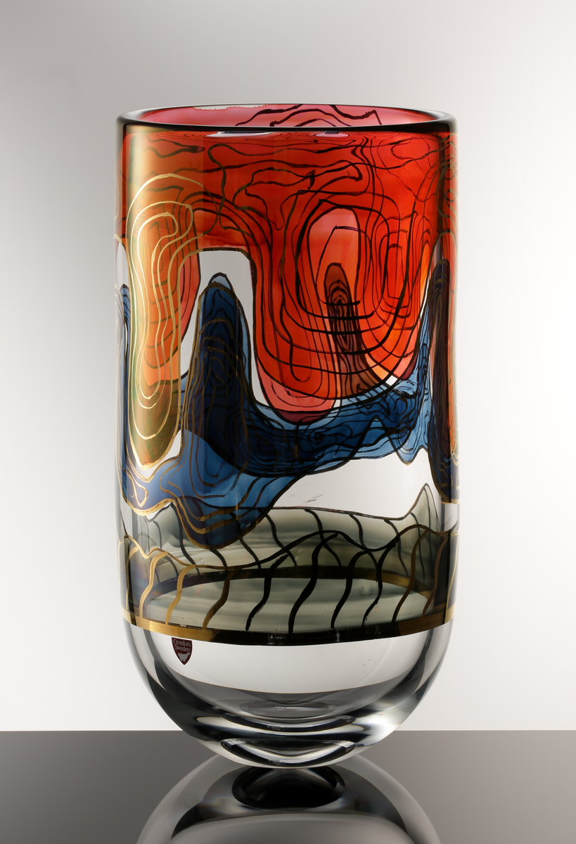 Formgivare: Jan Johansson. Cylindrisk vas i ofärgat glas med rundad bas. Målad abstrakt dekor i rött, blått och gråsvart, mönsterslingor i guld.