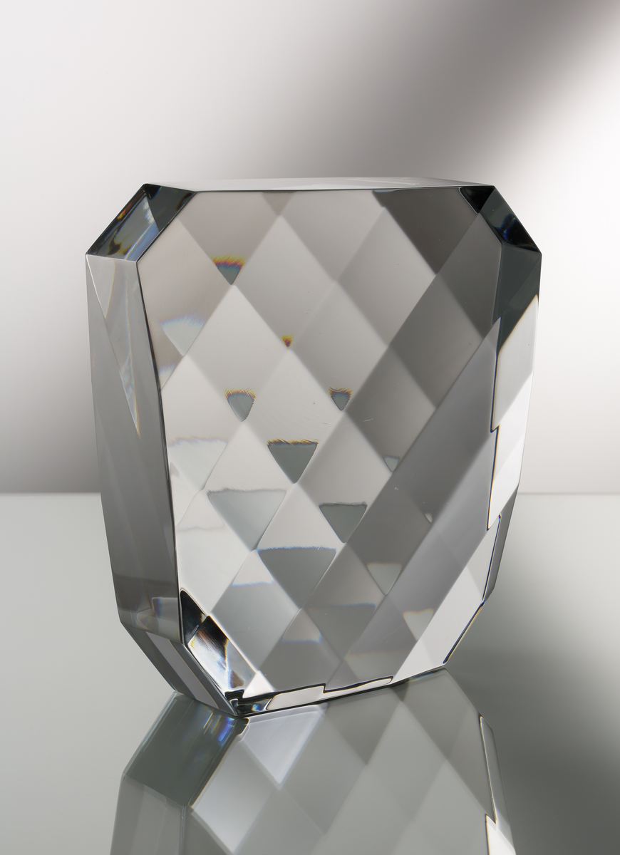 Formgivare: Jan Johansson. Skulptur i massivt klarglas. Rektangulär form med brutna hörn. Sju slipade diagonala fasetter på främre och bakre vägg som bildar ett "visuellt rutmönster".