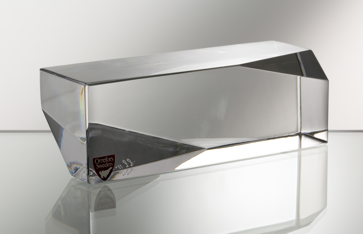 Formgivare: Jan Johansson. Skulptur "Jord". Massivt glas med rektangulär liggande form. Två diagonala hörn med triangulärt
slipad yta.