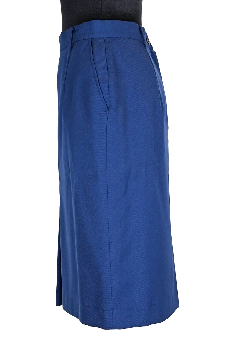 Kjol i mörkblå textil till ämbetsdräkt för kvinnlig personal vid Luftfartverket. Kjolen har två enkla framfickor. Längs midjan sitter fyra hällor för bälte. I bak i plaggets nederkant finns ett gångveck. Kjolen stängs i bak med dragkedja och knapp. Fodringen är mörkblå. 

På insidan i bak sitter två lappar med information om tillverkare och storlek. På ena lappen finns även Luftfartsverkets logga. Kjolen är producerad av Confetti i storlek C40. I en av hällorna sitter en papperslapp med nummer 8632. På denna har texten 3/10 påförts i bläck.