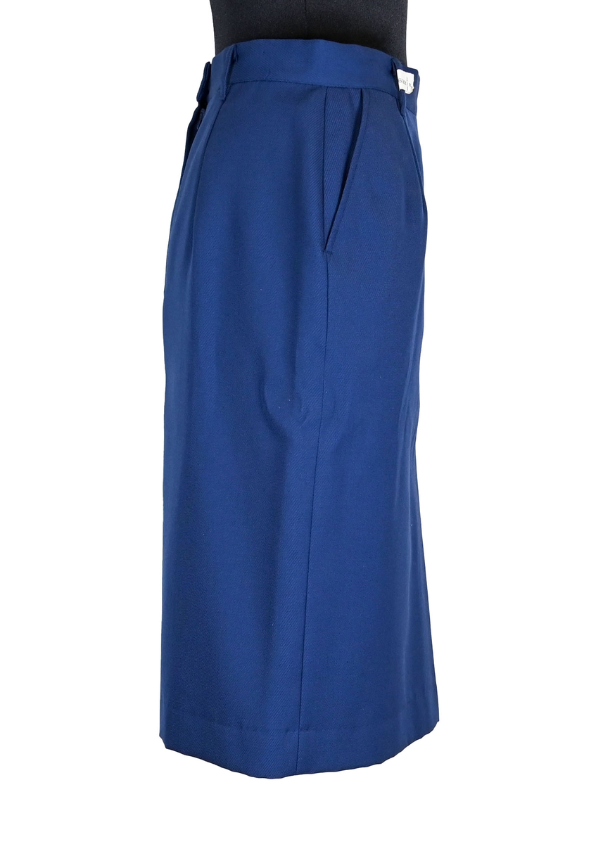 Kjol i mörkblå textil till ämbetsdräkt för kvinnlig personal vid Luftfartverket. Kjolen har två enkla framfickor. Längs midjan sitter fyra hällor för bälte. I bak i plaggets nederkant finns ett gångveck. Kjolen stängs i bak med dragkedja och knapp. Fodringen är mörkblå. 

På insidan i bak sitter två lappar med information om tillverkare och storlek. På ena lappen finns även Luftfartsverkets logga. Kjolen är producerad av Confetti i storlek C40. I en av hällorna sitter en papperslapp med nummer 8632. På denna har texten 3/10 påförts i bläck.