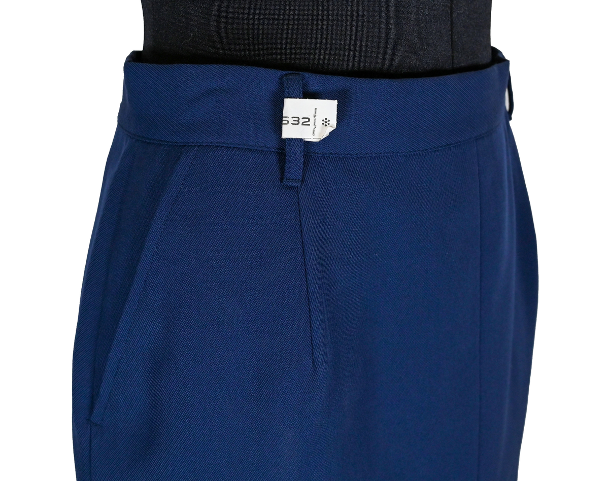 Kjol i mörkblå textil till ämbetsdräkt för kvinnlig personal vid Luftfartverket. Kjolen har två enkla framfickor. Längs midjan sitter fyra hällor för bälte. I bak i plaggets nederkant finns ett gångveck. Kjolen stängs i bak med dragkedja och knapp. Fodringen är mörkblå. 

På insidan i bak sitter två lappar med information om tillverkare och storlek. På ena lappen finns även Luftfartsverkets logga. Kjolen är producerad av Confetti i storlek C40. I en av hällorna sitter en papperslapp med nummer 8632. På denna har texten 3/10 påförts i bläck.