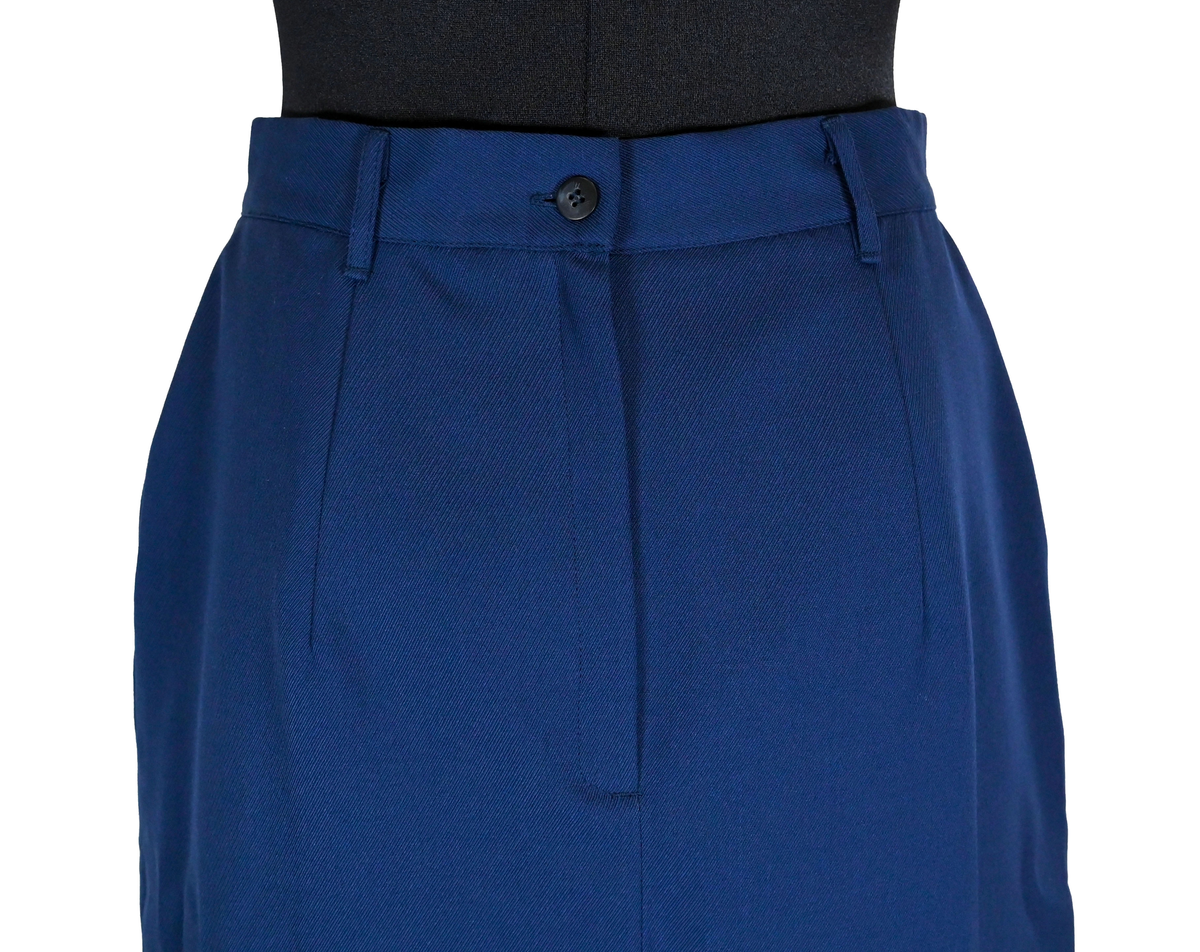 Kjol i mörkblå textil till ämbetsdräkt för kvinnlig personal vid Luftfartverket. Kjolen har två enkla framfickor. Längs midjan sitter fyra hällor för bälte. I bak i plaggets nederkant finns ett gångveck. Kjolen stängs i bak med dragkedja och knapp. Fodringen är mörkblå. 

På insidan i bak sitter två lappar med information om tillverkare och storlek. På ena lappen finns även Luftfartsverkets logga. Kjolen är producerad av Confetti i storlek C40. I en av hällorna sitter en papperslapp med nummer 8632. På denna har texten 3/10 påförts i bläck.